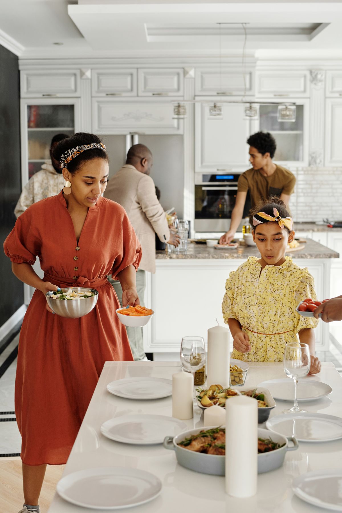 A family carrying dishes of food to a table in a modern kitchen