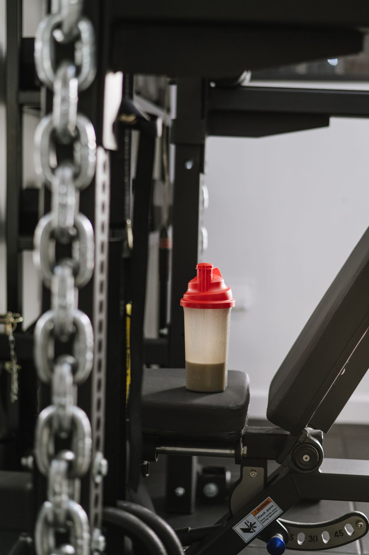 A shaker bottle resting on a gym bench beside weight stack chains