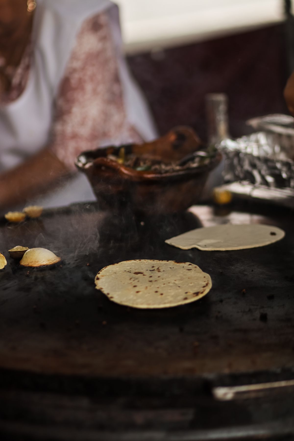 A street vendor cooking fresh corn tortillas on a hot griddle