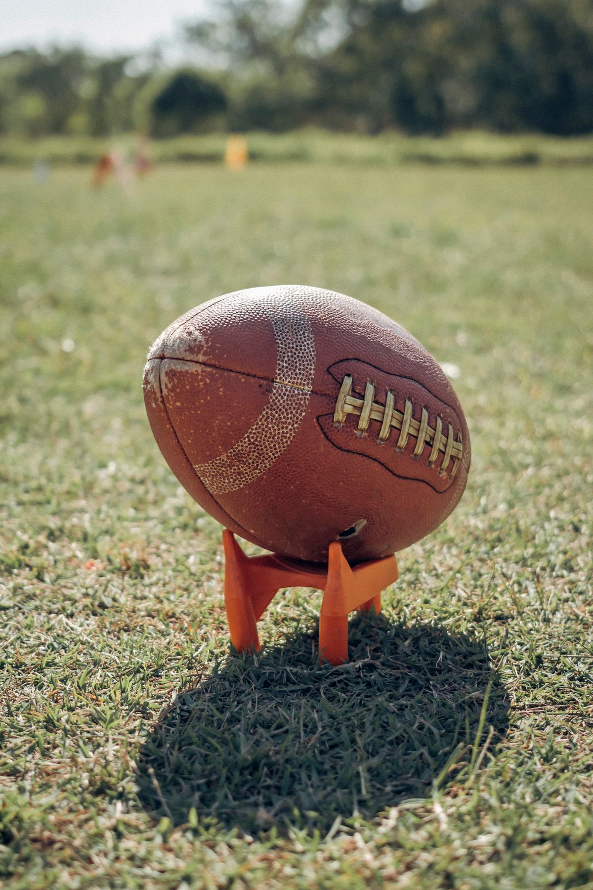 An American football resting on an orange kicking tee on a grass field